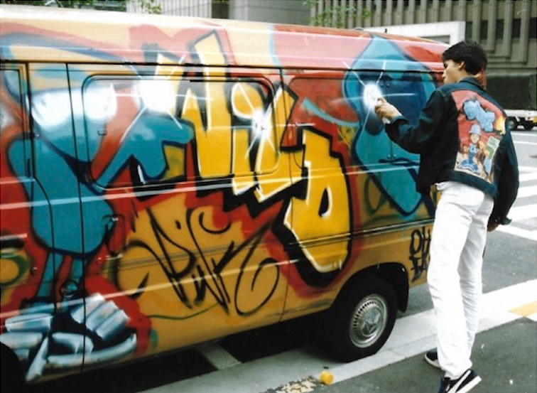 Devious Doze spray-painting a van covered in wild-style graffiti on a Japanese street
