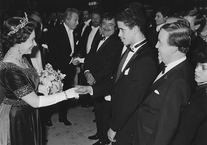 A young Crazy Legs in a tuxedo shakes hands with Queen Elizabeth II in a receiving line